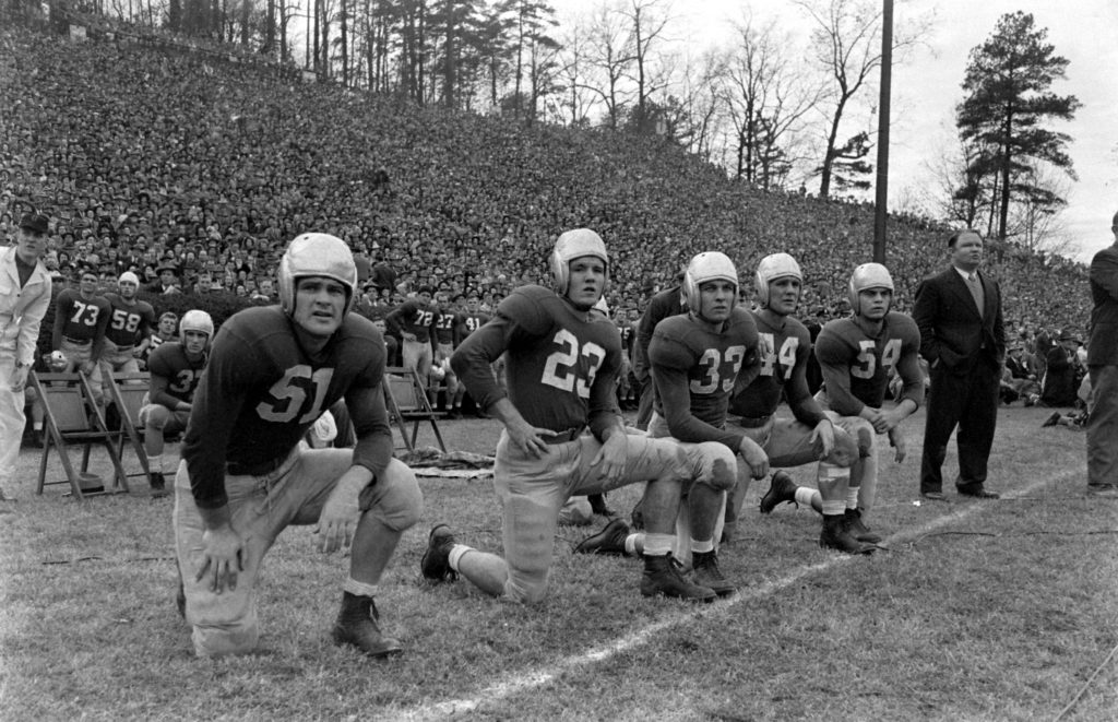 Historic football players kneeling along a crowded sideline